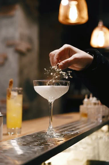 Bartender garnishing a white cocktail with delicate flowers in a coupe glass.