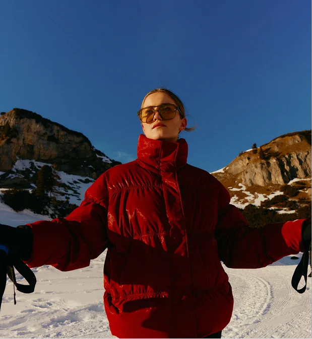 Woman in red ski jacket and sunglasses skiing downhill on a sunny day in the mountains.